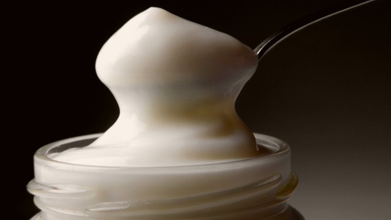 A spoon scooping mayonnaise out of a jar.